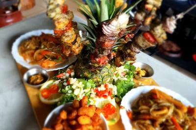 Assiette garnie de brochettes sur un ananas, accompagnée de légumes, sauces et bouchées frites.