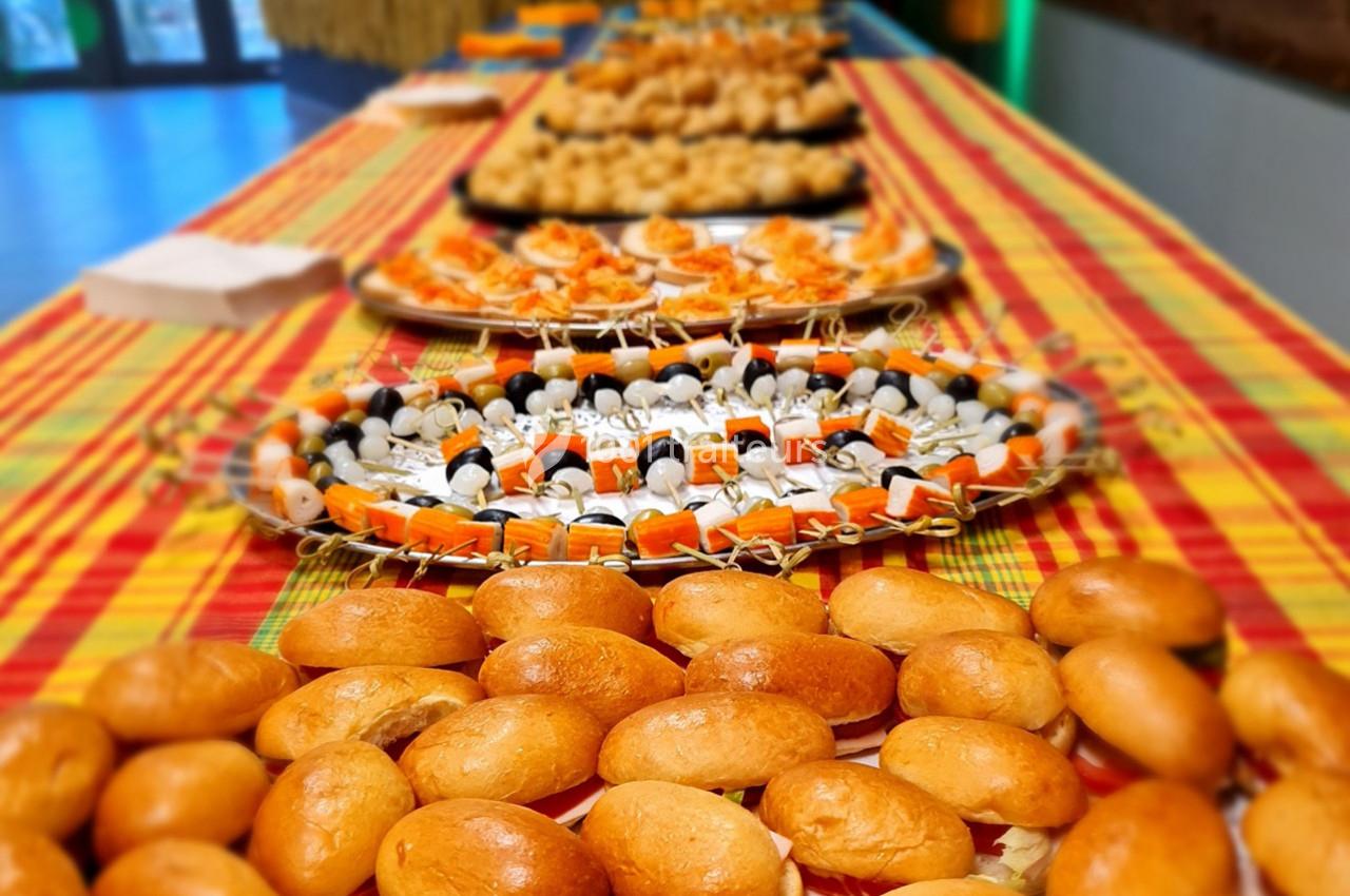 Plateau de buffet avec divers amuse-bouches, petits pains et brochettes, disposés sur une nappe colorée.