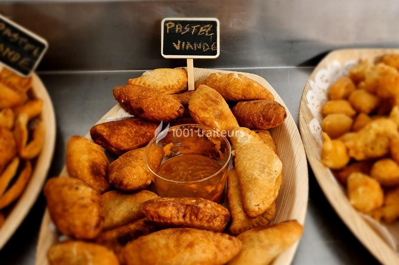 Assortiment de pastels à la viande dorés, accompagnés d'une sauce, présentés dans un plat en bois.