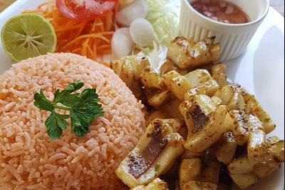 Assiette garnie de brochettes sur un ananas, accompagnée de légumes, sauces et bouchées frites.