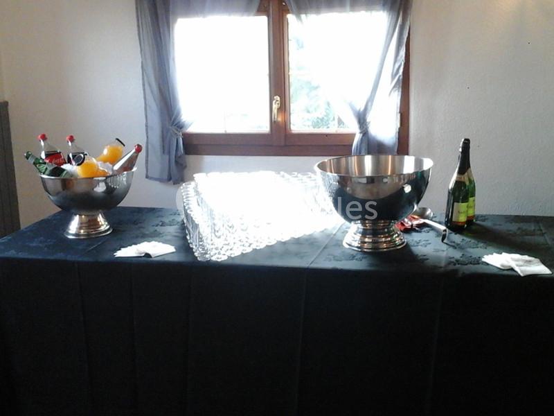 Table avec nappes noires, contenant des seaux remplis de boissons, des verres alignés et une bouteille de champagne.