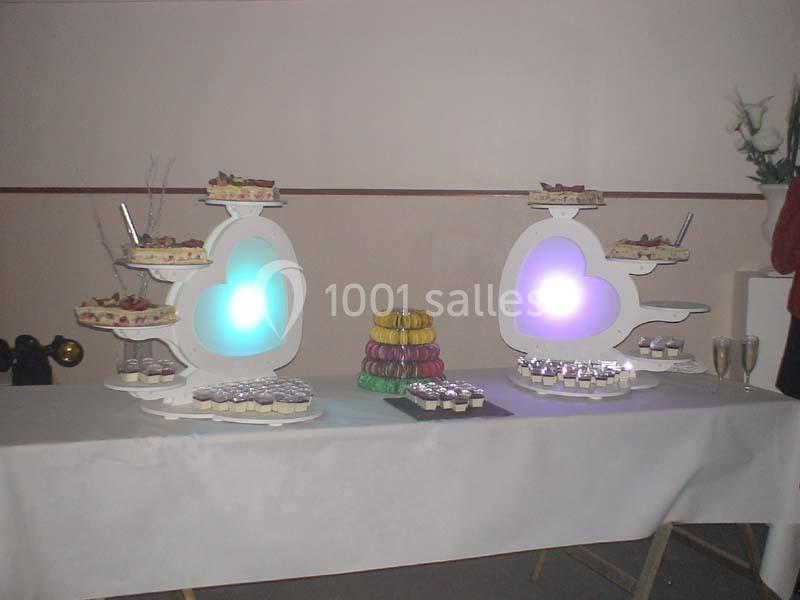 Table de réception avec présentoirs lumineux en forme de cœur, macarons colorés et verrines disposés sur une nappe blanche.