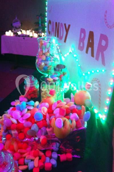 Bocaux remplis de bonbons colorés disposés sur une table décorée avec des lumières et un panneau ’Candy Bar’.