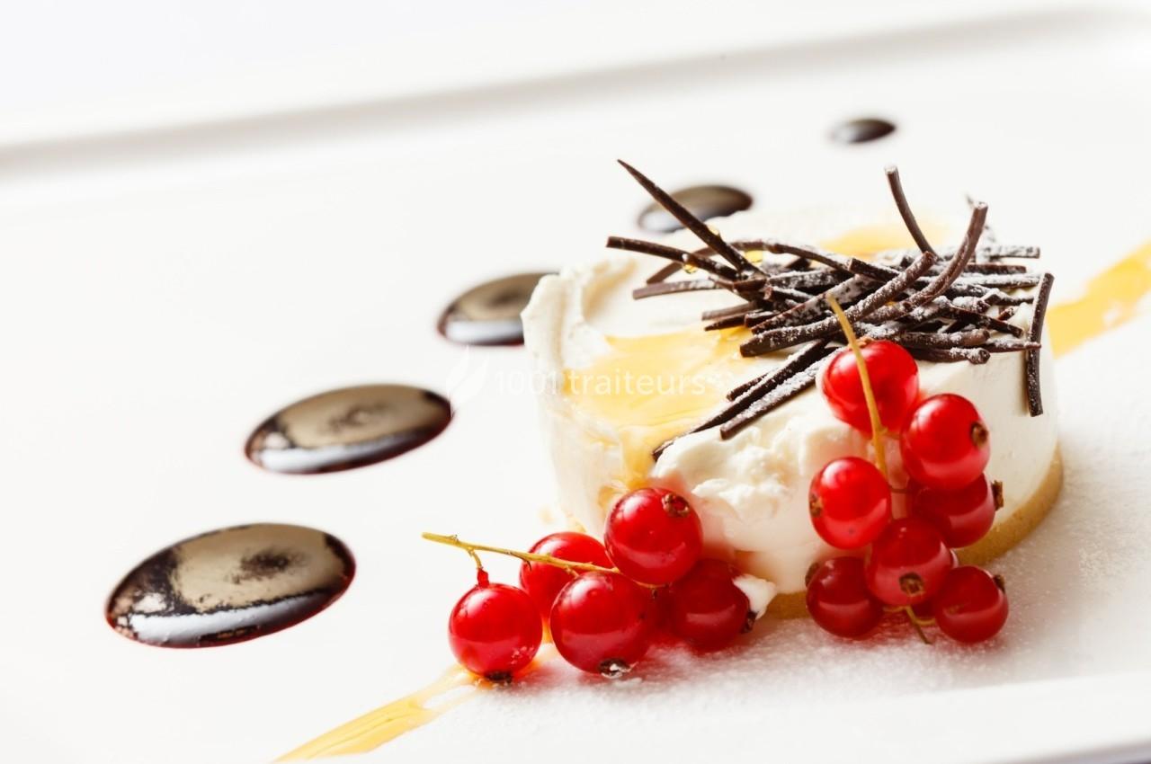 Dessert composé de fromage blanc, groseilles rouges, copeaux de chocolat et sauce décorative sur une assiette blanche.
