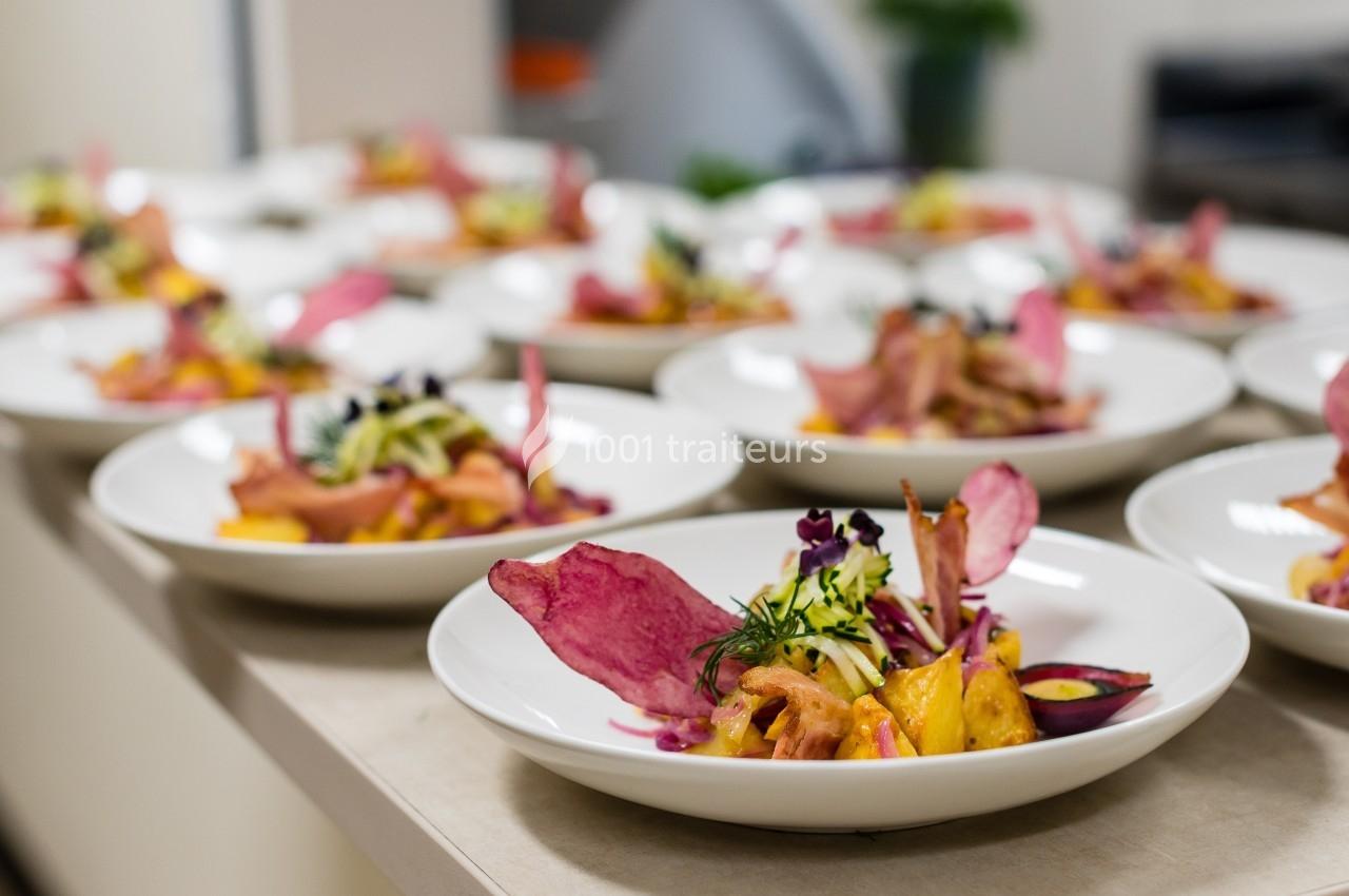 Assiettes de plats colorés avec légumes, chips de betterave et herbes fraîches alignées sur un plan de travail.