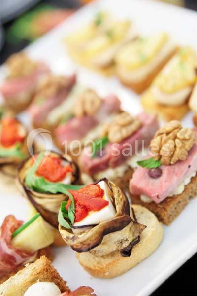 Assortiment de canapés variés garnis de légumes, noix, charcuteries et fromages sur un plateau blanc.