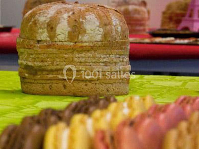 Pain artisanal sur une table verte, entouré de macarons colorés en premier plan et d'autres pâtisseries en arrière-plan.