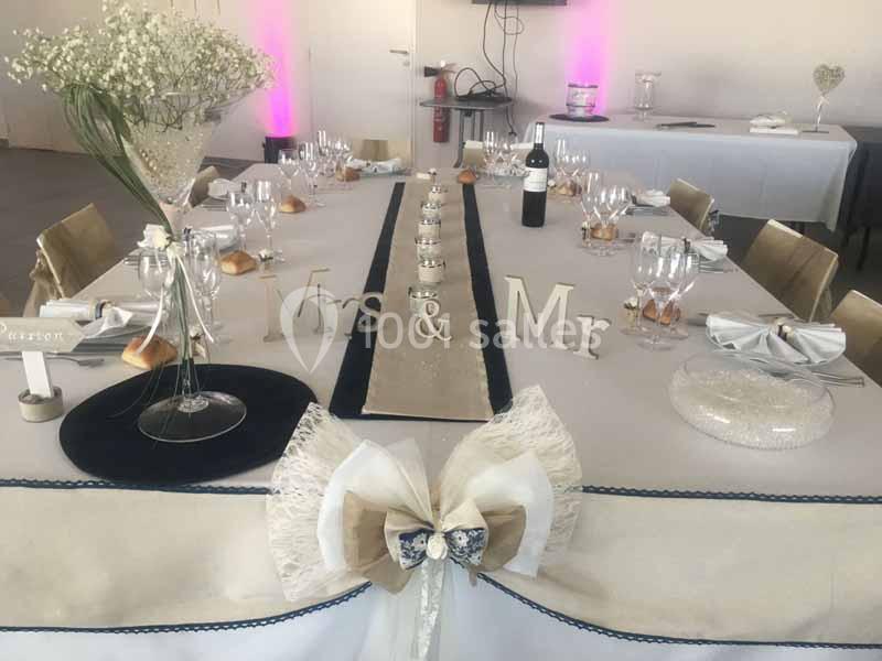 Table décorée pour un mariage avec nappes beige et blanche, vaisselle élégante, centre de table floral et lettres ’Mrs & Mr’.