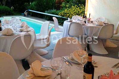 Centre de table floral avec roses et magnolias, bouteille de vin, numéro de table et décorations sur une nappe blanche.