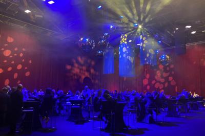Centre de table floral avec roses et magnolias, bouteille de vin, numéro de table et décorations sur une nappe blanche.
