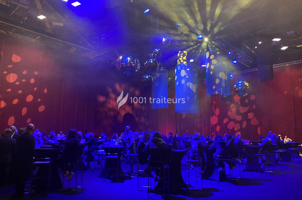 Salle de réception avec invités assis à des tables hautes, éclairée par des lumières colorées et des boules réfléchissantes.