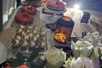 Centre de table floral avec roses et magnolias, bouteille de vin, numéro de table et décorations sur une nappe blanche.