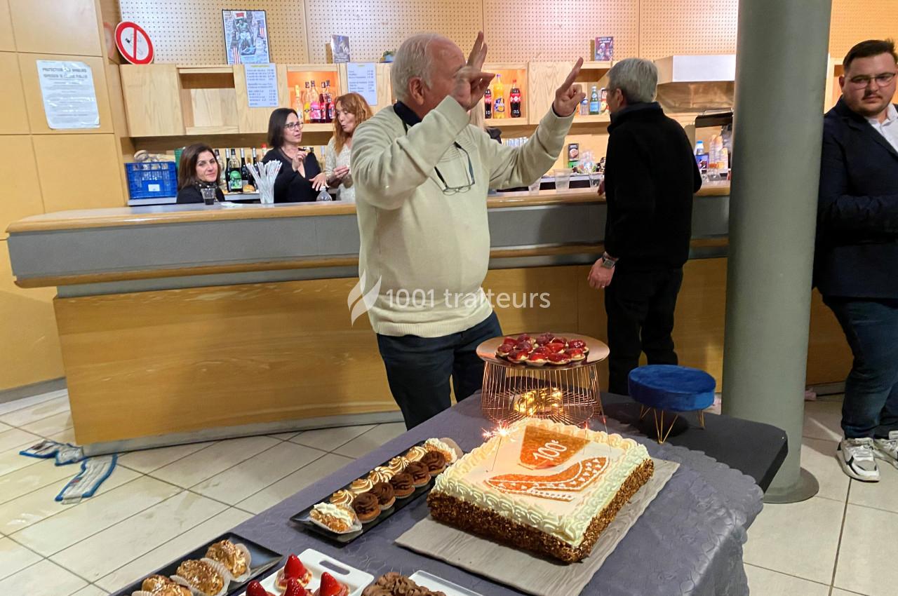 Un homme célèbre un anniversaire avec un gâteau décoré, entouré de desserts, dans une salle conviviale.