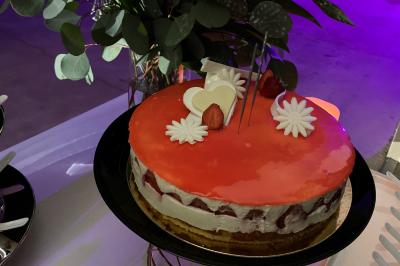 Centre de table floral avec roses et magnolias, bouteille de vin, numéro de table et décorations sur une nappe blanche.