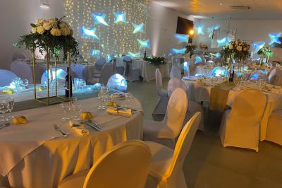 Centre de table floral avec roses et magnolias, bouteille de vin, numéro de table et décorations sur une nappe blanche.