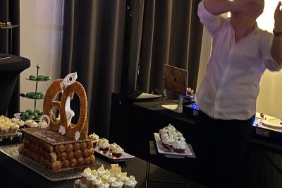 Centre de table floral avec roses et magnolias, bouteille de vin, numéro de table et décorations sur une nappe blanche.