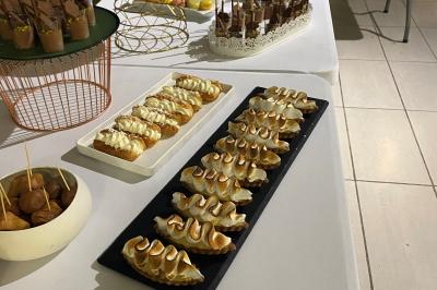 Centre de table floral avec roses et magnolias, bouteille de vin, numéro de table et décorations sur une nappe blanche.