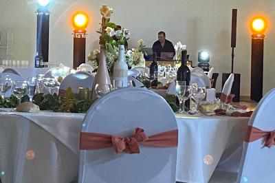 Centre de table floral avec roses et magnolias, bouteille de vin, numéro de table et décorations sur une nappe blanche.