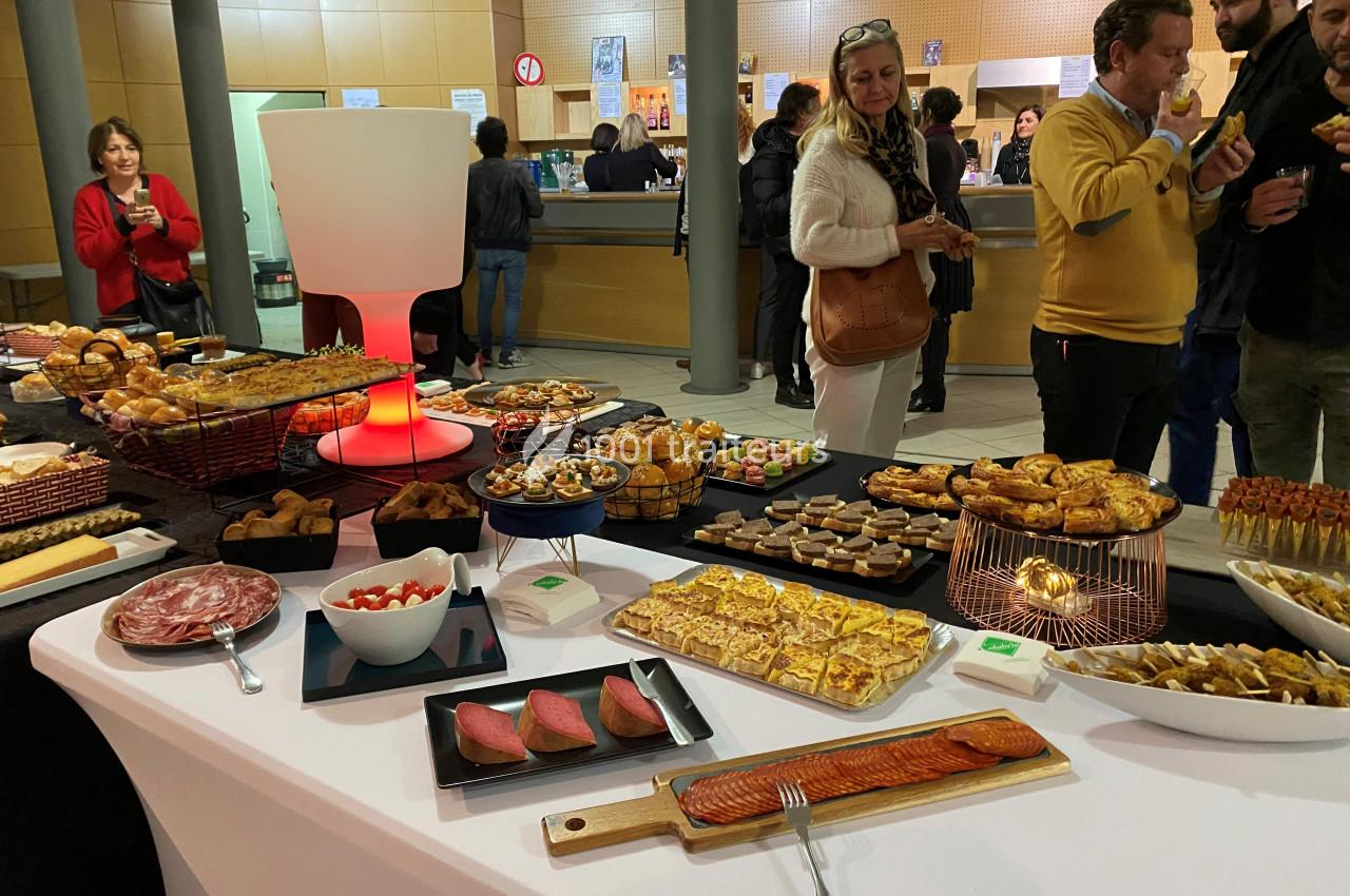 Buffet varié avec charcuterie, fromages, pâtisseries et amuse-bouches, dans un espace de réception animé.