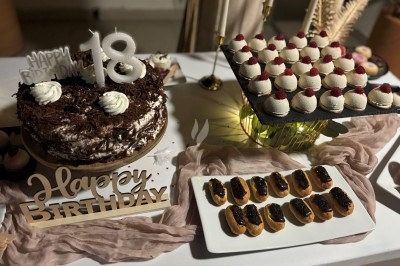 Centre de table floral avec roses et magnolias, bouteille de vin, numéro de table et décorations sur une nappe blanche.