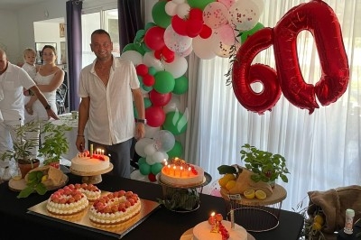 Centre de table floral avec roses et magnolias, bouteille de vin, numéro de table et décorations sur une nappe blanche.