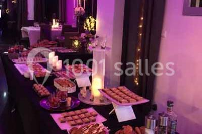 Centre de table floral avec roses et magnolias, bouteille de vin, numéro de table et décorations sur une nappe blanche.