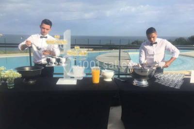 Centre de table floral avec roses et magnolias, bouteille de vin, numéro de table et décorations sur une nappe blanche.
