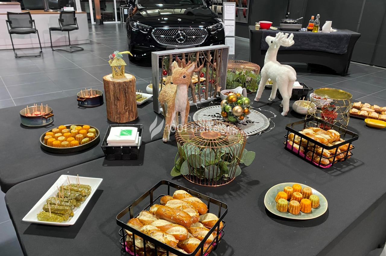 Buffet décoré avec des pâtisseries, amuse-bouches et ornements de Noël, dans un espace avec une voiture en arrière-plan.