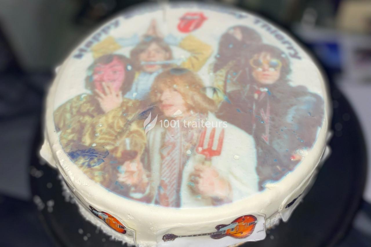 Gâteau décoré d'une image comestible représentant un groupe de musique, avec glaçage blanc et motifs de guitare.