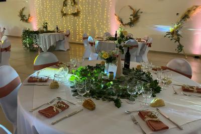Centre de table floral avec roses et magnolias, bouteille de vin, numéro de table et décorations sur une nappe blanche.