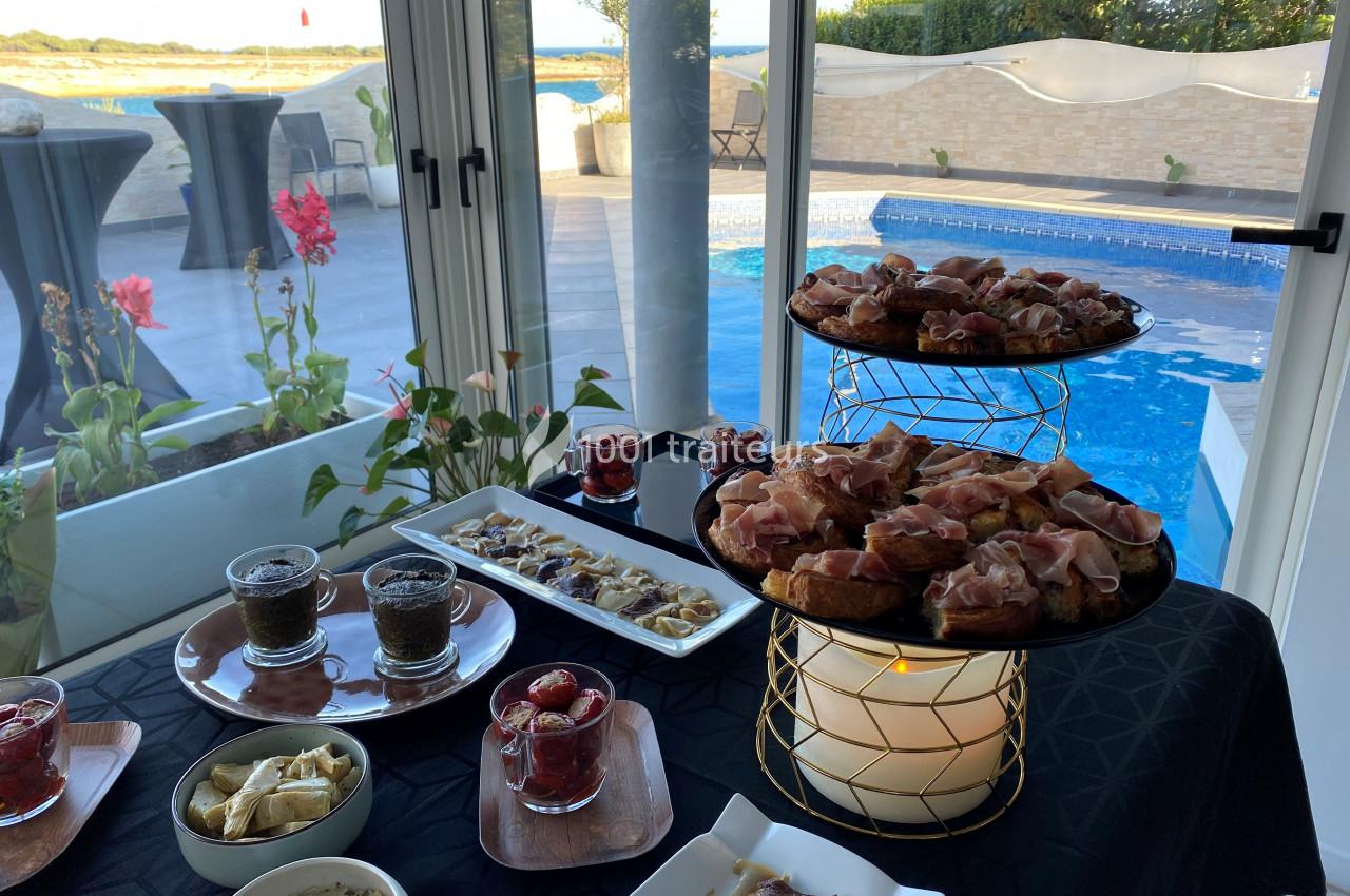 Buffet de hors-d'œuvre avec vue sur une piscine et une terrasse extérieure en arrière-plan.