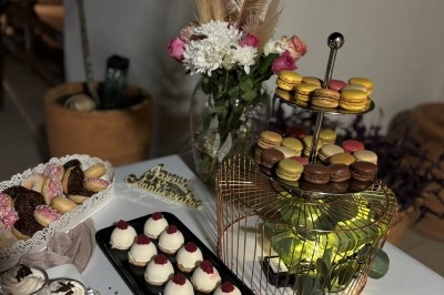 Centre de table floral avec roses et magnolias, bouteille de vin, numéro de table et décorations sur une nappe blanche.