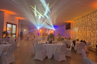 Centre de table floral avec roses et magnolias, bouteille de vin, numéro de table et décorations sur une nappe blanche.