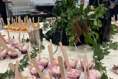 Groupe de personnes rassemblées en extérieur sous des arbres, près d'une table garnie de plats variés.