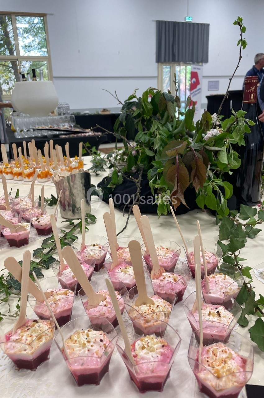 Desserts individuels à base de fruits rouges et crème, présentés sur une table décorée de feuillage et de bouteilles.