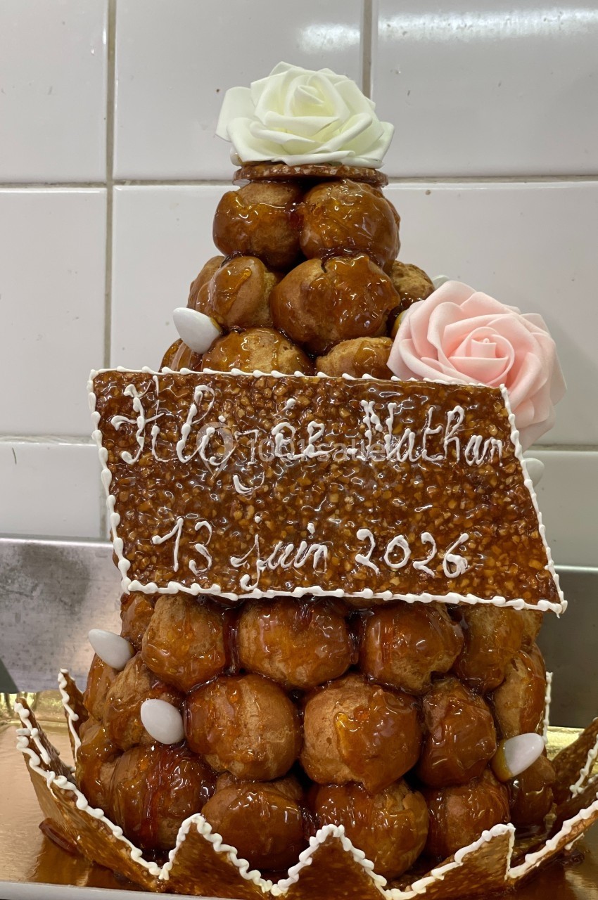 Pièce montée en choux caramélisés décorée de roses en sucre, avec une plaque indiquant ’13 juin 2026’.