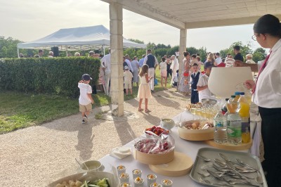 Groupe de personnes rassemblées en extérieur sous des arbres, près d'une table garnie de plats variés.