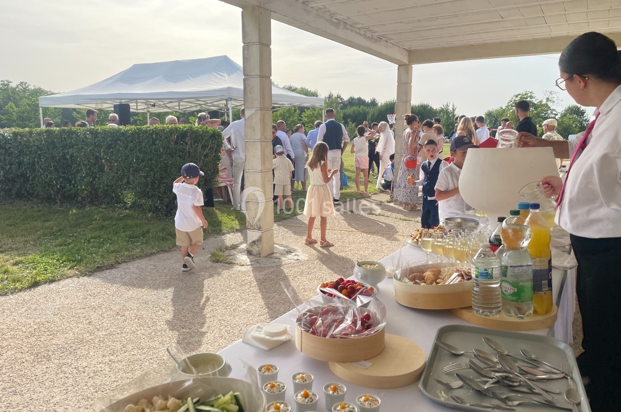 Buffet en plein air avec boissons et plats, des invités discutent sous une tente et des enfants jouent à proximité.