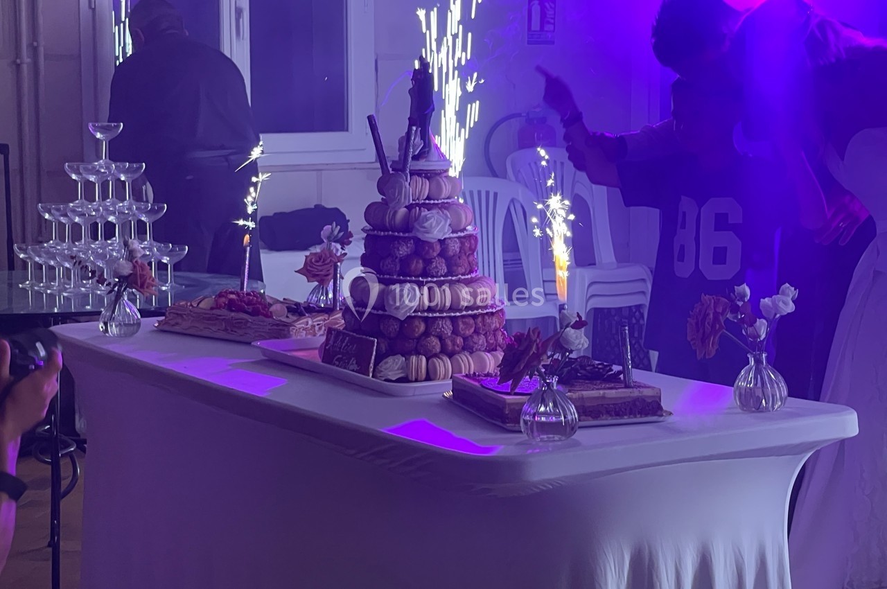Table de fête décorée avec une pièce montée de choux, des desserts, des fleurs et des fontaines lumineuses allumées.