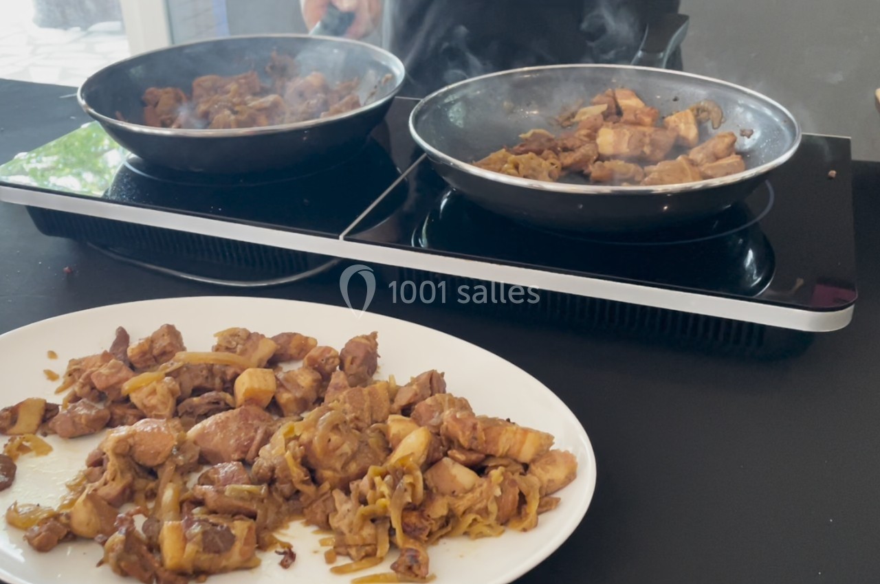 Morceaux de viande sautés avec des oignons dans deux poêles, servis sur une assiette blanche au premier plan.