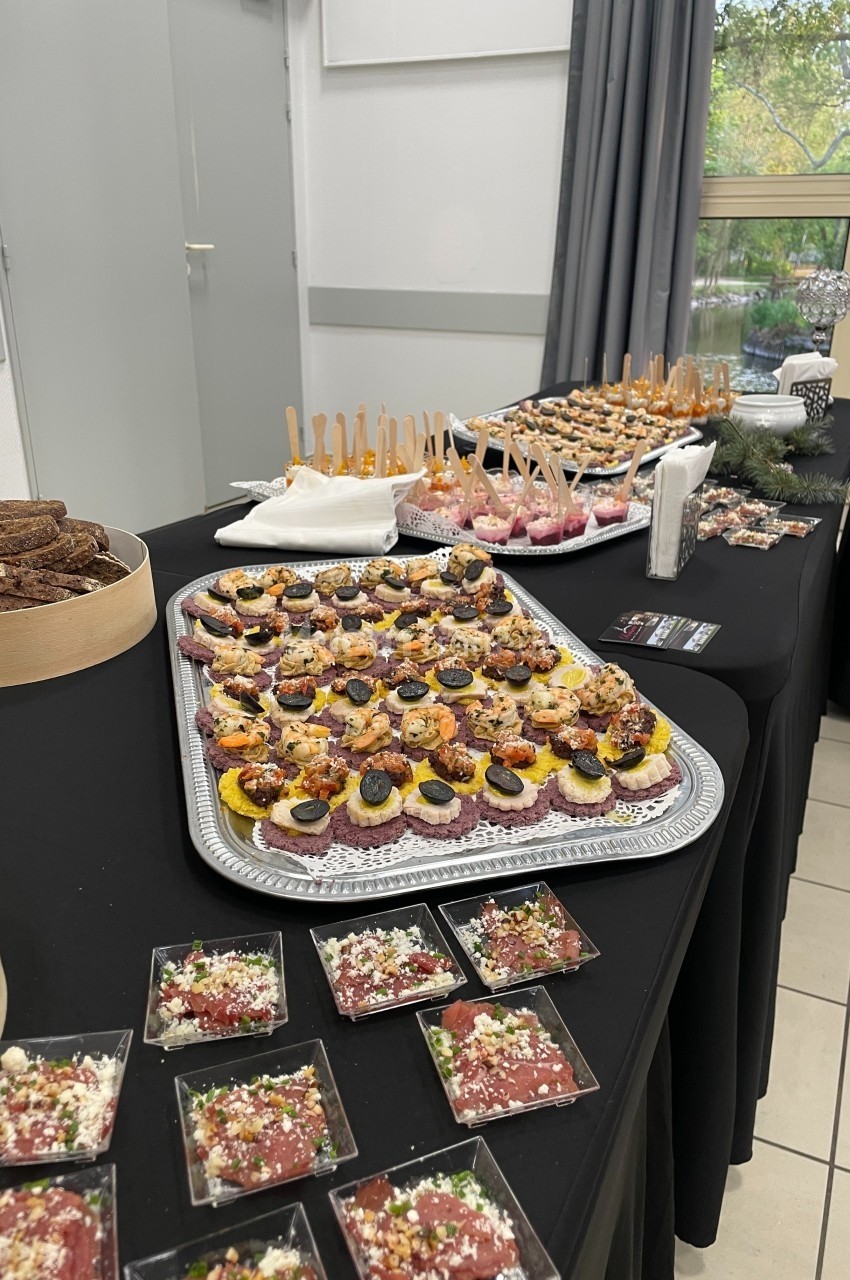 Plateau de canapés variés et verrines disposés sur une table noire lors d'un buffet en intérieur.