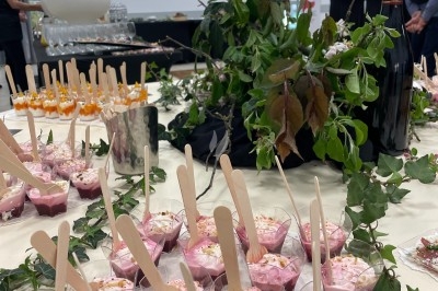 Groupe de personnes rassemblées en extérieur sous des arbres, près d'une table garnie de plats variés.