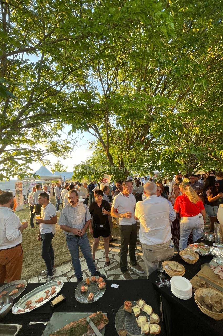 Groupe de personnes rassemblées en extérieur sous des arbres, près d'une table garnie de plats variés.