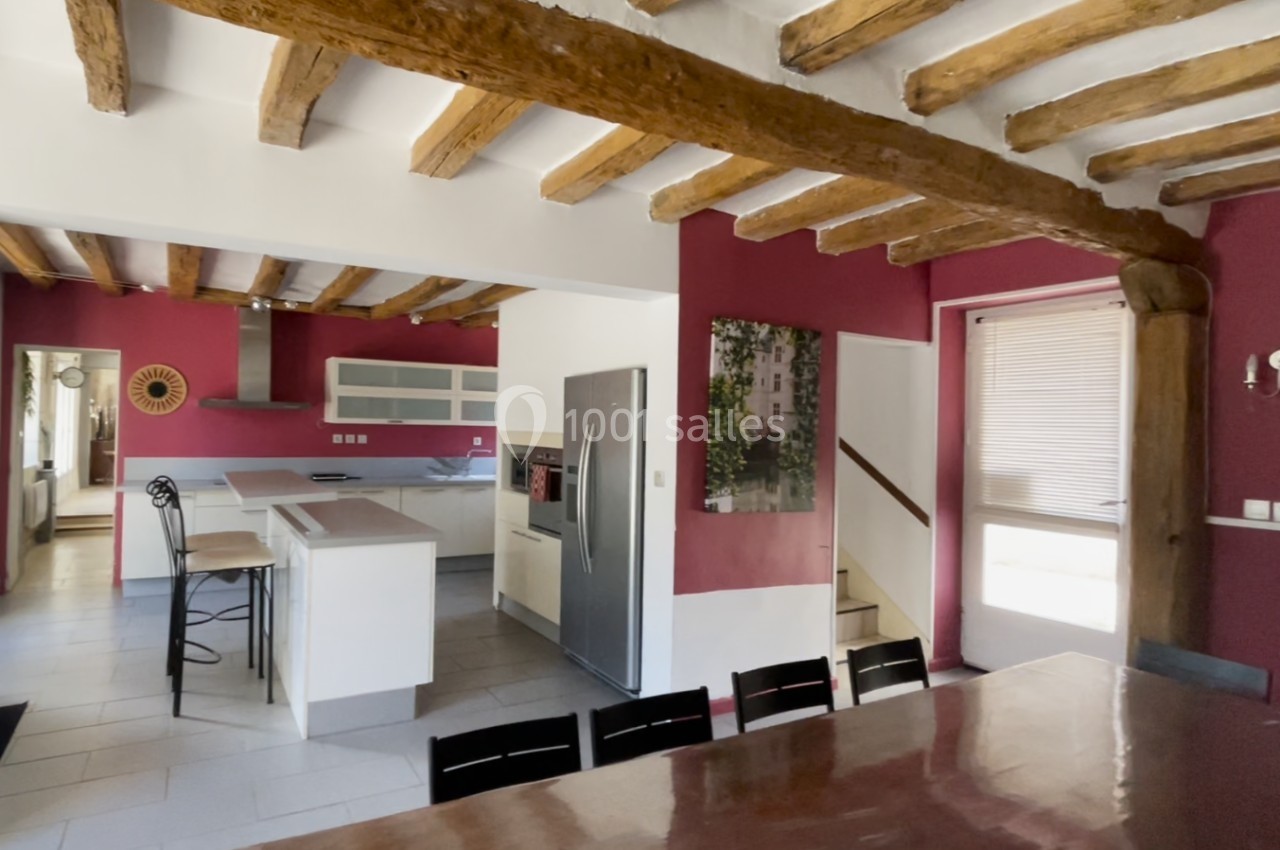 Cuisine ouverte avec poutres apparentes, murs rouges, îlot central, électroménagers modernes et table en bois.