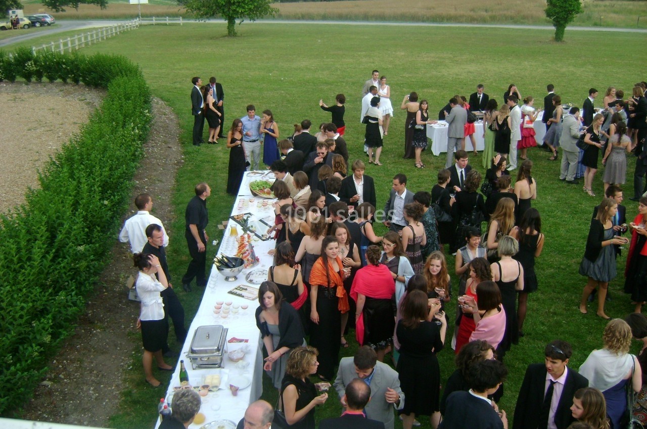 Groupe de personnes rassemblées autour de tables lors d'une réception en plein air sur une pelouse.