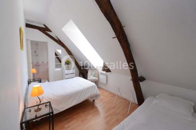 Chambre mansardée avec deux lits simples, parquet clair, poutres apparentes et lumière naturelle provenant d'un velux.