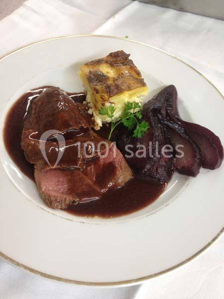 Assiette contenant une tranche de viande nappée de sauce, une poire au vin rouge et un gratin de pommes de terre.