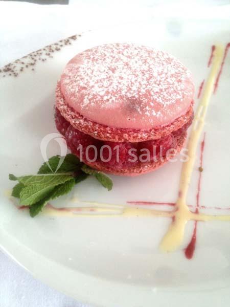 Macaron rose garni de framboises fraîches, posé sur une assiette décorée de coulis et accompagné de feuilles de menthe.