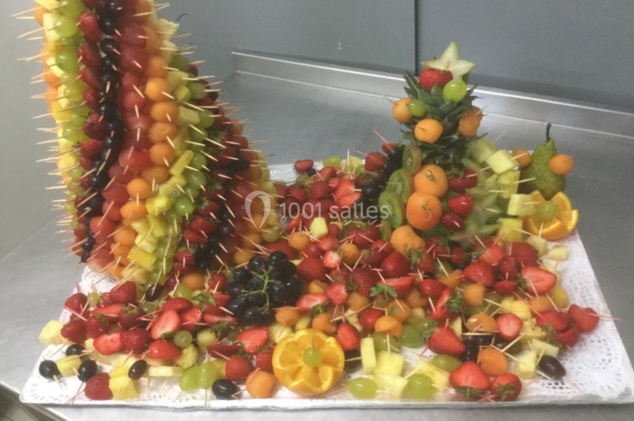 Présentoir de brochettes de fruits variés avec fraises, raisins, oranges et autres fruits colorés sur une table.