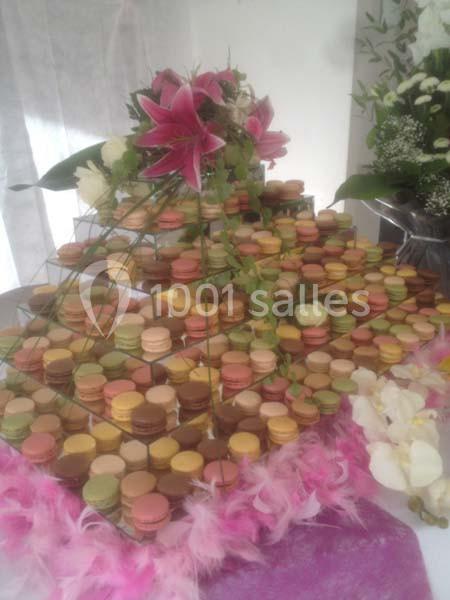 Tour de macarons colorés décorée de fleurs et de feuillage, présentée sur une table avec des plumes roses.